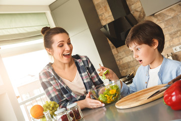Family at home standing in kitchen together looking at spoon with salad laughing surprised