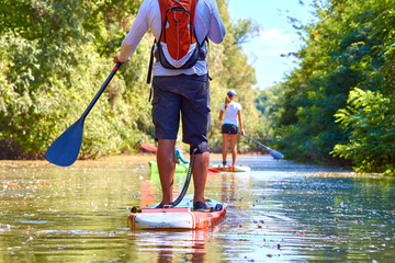 Close-up of a woman and man legs on stand up paddle in water - obrazy, fototapety, plakaty