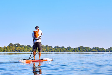 Athletic man paddling on stand up paddle board (paddleboard, SUP) in Danube river at summer