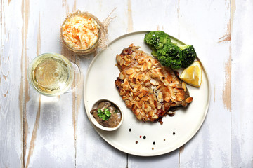 Karp z migdałami.  Smażony karp w panierce z płatków migdałowych, podany z brokułem, surówką z białej kapusty i kieliszkiem wina. © foodandcook