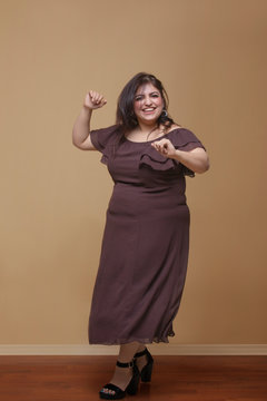 Fat woman in a long brown dress dancing on high heels	