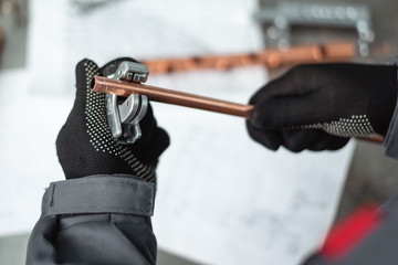 Engineer is holding in hands a pipe cutter tool on a factory workbench background.