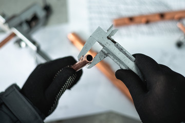 Engineer is holding in hands a brass pipe and is measuring a diameter by a calipers. Pipework.