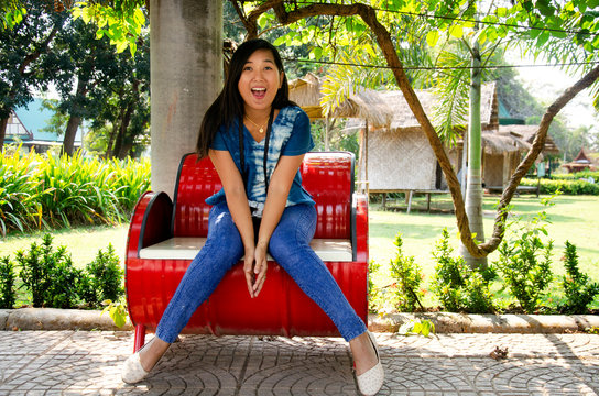 Asia thai woman travel visit and sitting on red metal bench posing for take photo in public garden park