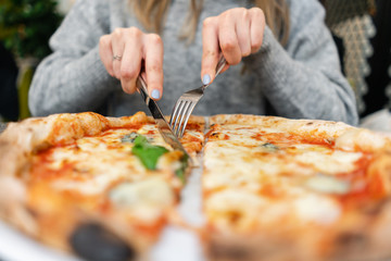 Woman eats with knife and fork a pizza Margherita with mozzarella tomatoes and basil. Neapolitan...