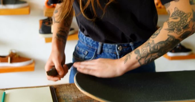 Front view of young caucasian woman applying skateboard grip tape in workshop 4k