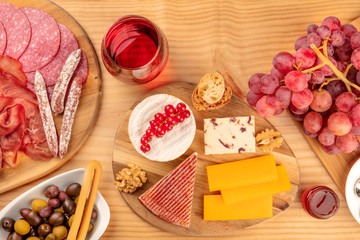 A charcuterie platter and a cheese board, sausages and hams, and a glass of red wine, shot from the top on a wooden background with copy space