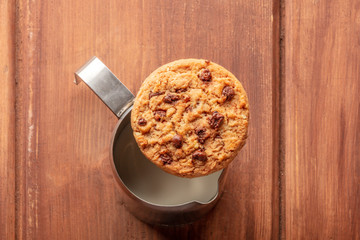 Good morning. A chocolate chip cookie, shot from above on top of a milk jug, on a dark rustic wooden table with a place for text