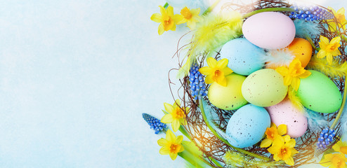 Colorful Easter eggs in nest and spring flowers on rustic table top view. Holiday card or banner.