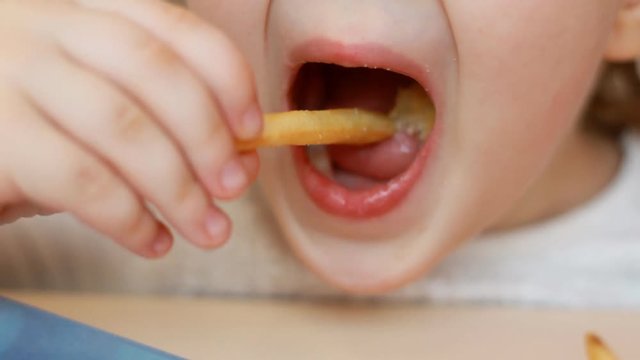 Child eating french fries closeup. Portrait of a baby who eats fast food
