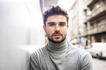 young guy with beard posing on gray wall