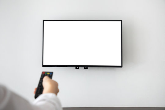 human hand pressing remote control with blank screen television on concrete wall at living room.