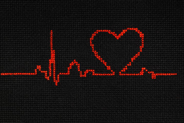 Cardiogram with a heart symbol is embroidered with red thread on a black cloth.