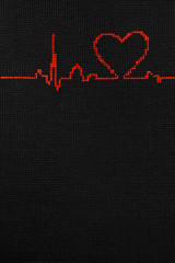 Cardiogram with a heart symbol is embroidered with red thread on a black cloth.