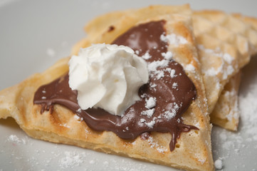 closeup of waffle in shaped heart with chocolate and chantilly cream in a white plate