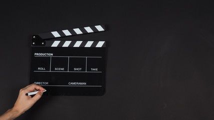 Fototapeta na wymiar Black Clapperboard or clap board or movie slate with left hand holding pen use in video production ,film, cinema industry on black background.