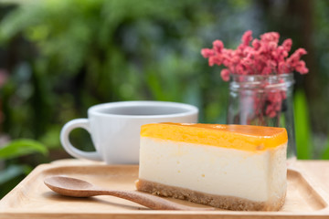 Passion fruit cheesecake and hot coffee cup on wooden tray and table with green nature background