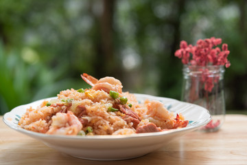 Delicious Thai fried rice with shrimp on wooden table with beauitful vase ,green blurred background