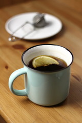 Hot warming tea with lemon in a light blue mug with a brewed tea strainer on a table with a wooden texture