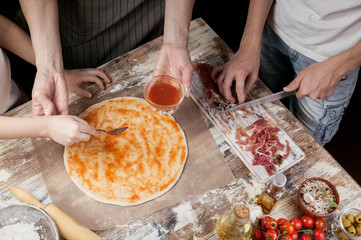 Cooking pizza with mom. Mom and her children make delicious pizza with prosciutto and cherry tomatoes. Food concept.