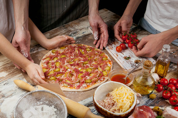 Cooking pizza with mom. Mom and her children make delicious pizza with prosciutto and cherry tomatoes. Food concept.