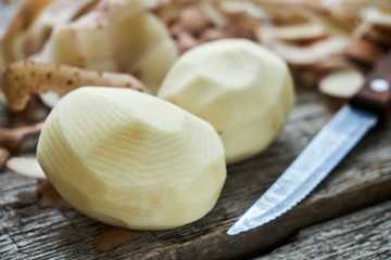 Fototapeta na wymiar Peeled potatoes with a knife and potato peel on the rough wooden a country table