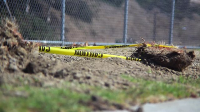 An empty desolate park enclosed by a chain link fence where the wind blows caution tape attached to a dirt rock.
