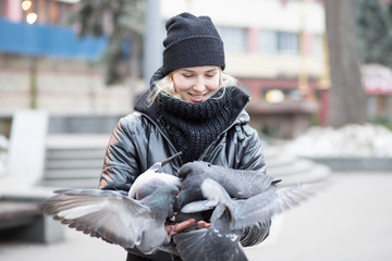 Birds doves eat sunflower seeds from the hands of a beautiful young girl in a black jacket and hat...