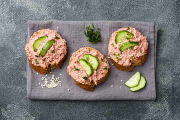 Sandwiches with chicken pate and cucumber on dark table.