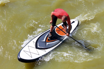 Standup paddle board surfer (SUP) surfing on wave at stormy lake at windy day