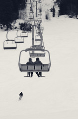 Two skiers on chair-lift in gray winter day