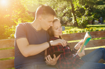 Naklejka premium man with tablet in his hands reads an interesting place in book that girl held in his hands next to him