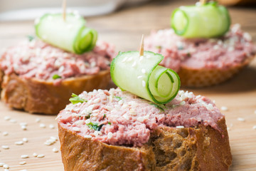 Sandwiches with chicken pate and cucumber on wooden table.