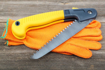 Folding garden saw with work gloves on wooden