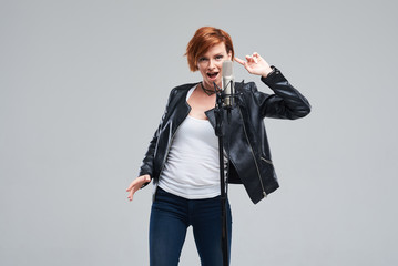 Portrait of rock singer wearing leather jacket and keeping static mic, sings a song loudly on grey...