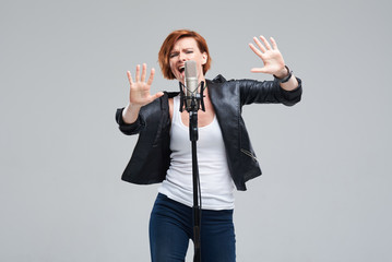 Portrait of rock singer wearing leather jacket and keeping static mic, sings a song loudly on grey...