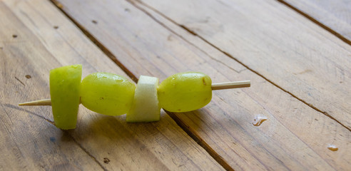 Fresh fruit pieces on a wooden skewer on a wood table top image with copy space in landscape format