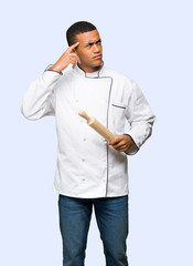 Young afro american chef man having doubts while scratching head on isolated background