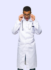 Young afro american man doctor with glasses and surprised on isolated background