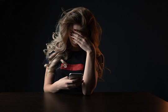 Closeup picture of frustrated girl, young woman being a victim of bullying online sitting isolated over the black backgrownd
