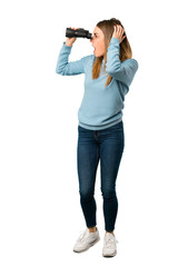 Full body of Blonde woman with blue shirt and looking in the distance with binoculars on white background