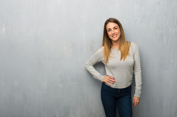 Young woman on textured wall posing with arms at hip and smiling