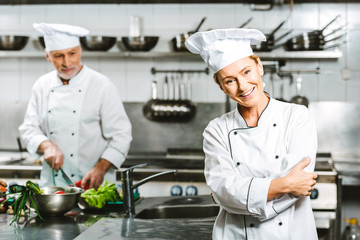 beautiful female cook and male chef in double-breasted jackets during cooking in restaurant kitchen