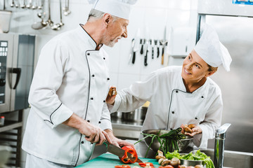 female and male chefs in uniform and hats cooking in restaurant kitchen