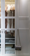Wardrobe with stylish bag and clothes indoors. Clothes hanging on rail in white wardrobe with boxes.