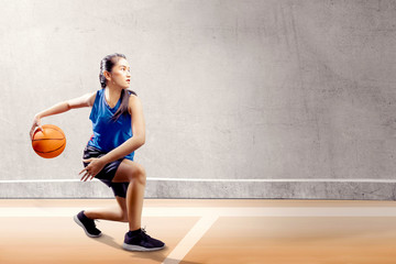 Attractive asian girl in blue sport uniform on basketball pivot moves on the basketball court