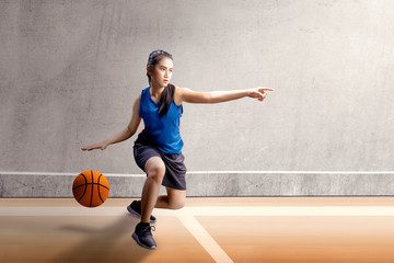 Beautiful asian woman in sport jersey dribbling the basketball with left arm pointing in the...