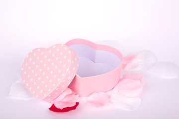 pink gift box with white polka dots and heart shape on white background and petals 