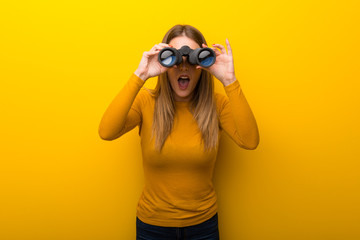 Young woman on yellow background and looking in the distance with binoculars