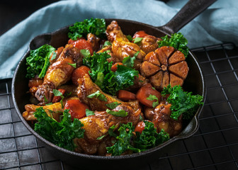 Roasted chicken wings with carrots, kale, garlic and dipping sauce in iron pan on dark background. Space for text.